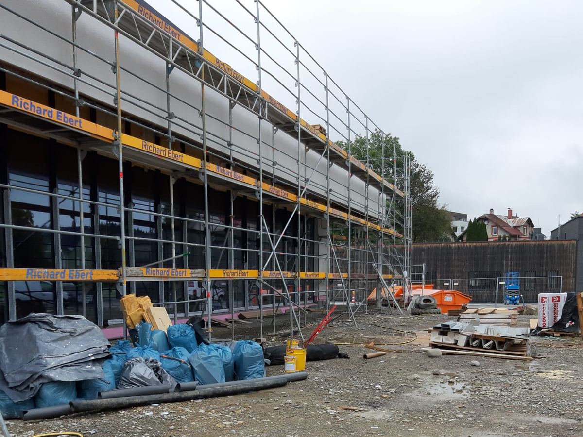 Neubau mit Baugerüst, davor ein aufgeräumtes Baufeld mit gefüllten Bauschuttsäcken