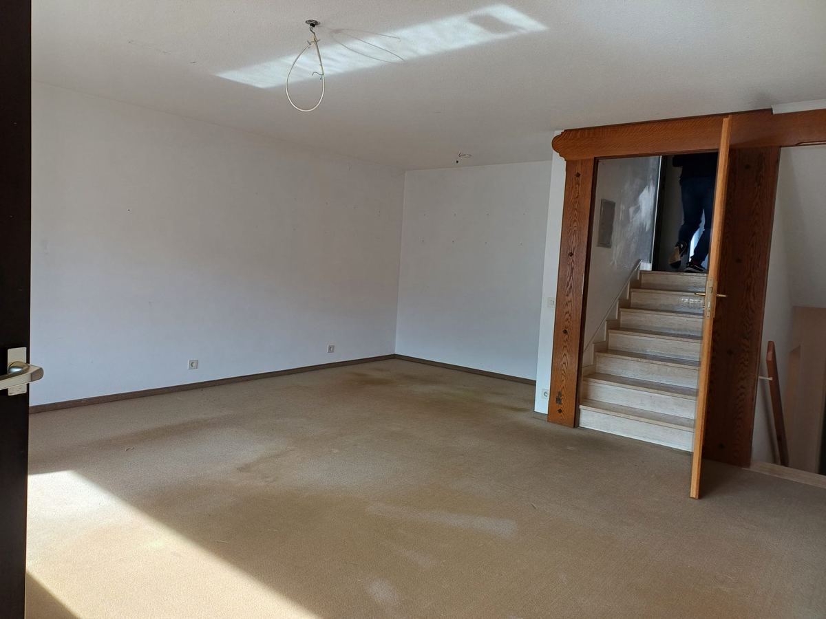 Leer geräumter Wohnraum mit Treppenaufgang und sauberem Boden